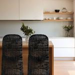 Two Sway rattan bar stools at wooden kitchen island with modern white cabinetry and decorative plants