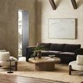 Painting displayed on beige plaster wall in modern living room with dark brown velvet sofa and round wood coffee table