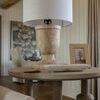 Table lamp on round wooden table in living room with beige couch and framed artwork behind