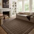 Bradley Cocoa rug styled in a living room with varied light, under sofa and chair on herringbone wood floor