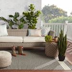 Outdoor porch setting with striped rug under wicker sofa and green plants
