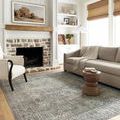 Living room vignette with sofa and armchair arranged on rug near white lamps and windows with bamboo blinds.