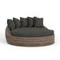 Round outdoor daybed with aged tobacco all-weather wicker frame and dark plush cushions and pillows