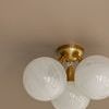 Flush mount with white globes and brass canopy viewed at an angle showing light reflection and ceiling detail