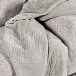Throw blanket casually draped over arm of textured gray sofa showcasing fabric drape and sherpa lining