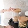 Hand placing a large wood top canister filled with rice onto a black round tray with a concrete background