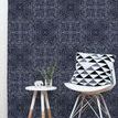 Wallpaper installed on wall behind white chair with black and white geometric pillow and small table on wooden floor
