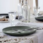 Side angle of artichoke plate on table with silver fork and knife, set against blurred casual dining setup
