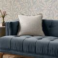 Pillow placed on tufted blue velvet couch against leaf-patterned wallpaper in room setting