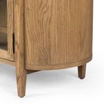 Detailed view of the curve of the side panel and the tapered wooden leg beneath the glass door