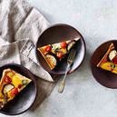 three plates styled with vegetable tart slices on a textured light surface with a beige linen napkin