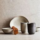 Styled group of bowls and cups including breakfast glaze bowl on textured surface