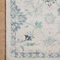 Close-up of the rug’s corner on wood floor highlighting intricate blue and ivory pattern and fabric weave.