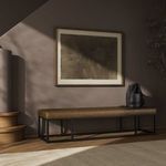 Bench in dimly lit room with wall art above and black bag on leather seat