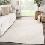 Ivory rug styled in a bright living room with white sofa, side table, and potted plants