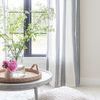 Soft textured area rug under a gray coffee table with woven tray, pink flowers, and striped curtains in bright room