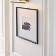 Close-up side view of 18 inch brass picture light highlighting framed artwork on paneled wall