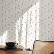 Miniature roses wallpaper applied on wall behind wooden desk and cane chair in bright room