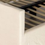 Detail of upholstered linen footboard corner with visible stitching and wooden slat bed frame beneath