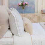Styled bedroom scene with duvet set, blush and beige pillows, vase with pink flowers, and light wood furniture