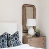 Wingback bed in a light bedroom with dark blue patterned pillows and rustic mirror on nightstand