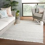 Close-up of light gray and cream textured weave of Torre rug with green tropical leaves on glass vase