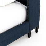 Brass-finished nailhead trim along winged side of indigo upholstered headboard