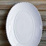 Close-up top view of white oval platter highlighting scalloped pearl edge against weathered wood background