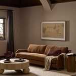 Styled room scene with Lynne Sofa, a round white coffee table, side table, and framed painting on beige walls.