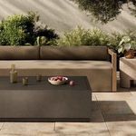 Outdoor setting with the coffee table placed in front of a brown cushioned sofa with decorative items on top