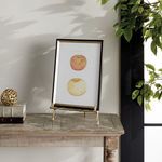 Baldwin Easel holding framed art on wooden table in sunlit room with leafy plant