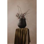 Black vessel styled with dried branches and red berries on a draped olive-green cloth