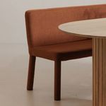 Close-up of banquette in room setting showing rounded legs and upholstery beside light wood table edge