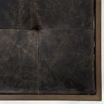Extreme close-up of leather tuft and stitch detail with bronze-toned metal border