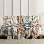 Multiple striped linen throws in assorted neutral and pastel colors draped over sectional sofa with fringed edges visible