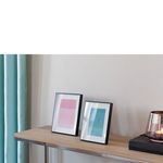Two black picture frames on a wooden shelf against white wall, paired with teal curtain and glass candle holder