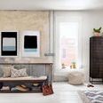 Bright airy room with paired Modern abstract paintings above rustic bench and pouf near window and dark wood cabinet