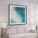 Angled view of coastal print above sofa showing depth and surrounding minimalist decor