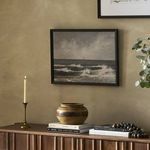 Painting hanging on beige wall above wooden sideboard with candle, pottery, and decor