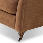 Close-up of brown fabric Lynne Chair showing front caster detail on turned wood leg
