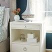 Frances side table styled by bed with white ceramic lamp and books on shelf alongside floral arrangement