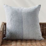Otis Pinstripe Pillow styled upright on a woven rattan chair against a light wall.
