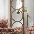 Tall floor mirror with a rustic wooden frame featuring three large circular cutouts, leaning against a white wall between ...