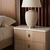 Nightstand detail showing textured drawer fronts, brass hardware, and beige lamp on marble top