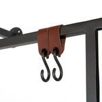 Close-up of two adjacent black metal hooks attached with brown leather straps on gunmetal frame