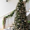 angled side view of fully decorated Christmas tree with staircase and garland in background
