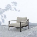 Sherwood Outdoor Faye Ash Bronze Chair angled outdoors on stone tiles with shadowed wall background