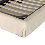 Close-up of bed frame corner showing cream linen slipcover with tailored side vents