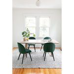 Dining table presented in a minimal room with green chairs arranged around the table on a gray rug