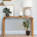 Console table styled in a room with decorative vases and lamp on top, and a potted plant underneath against a light wall